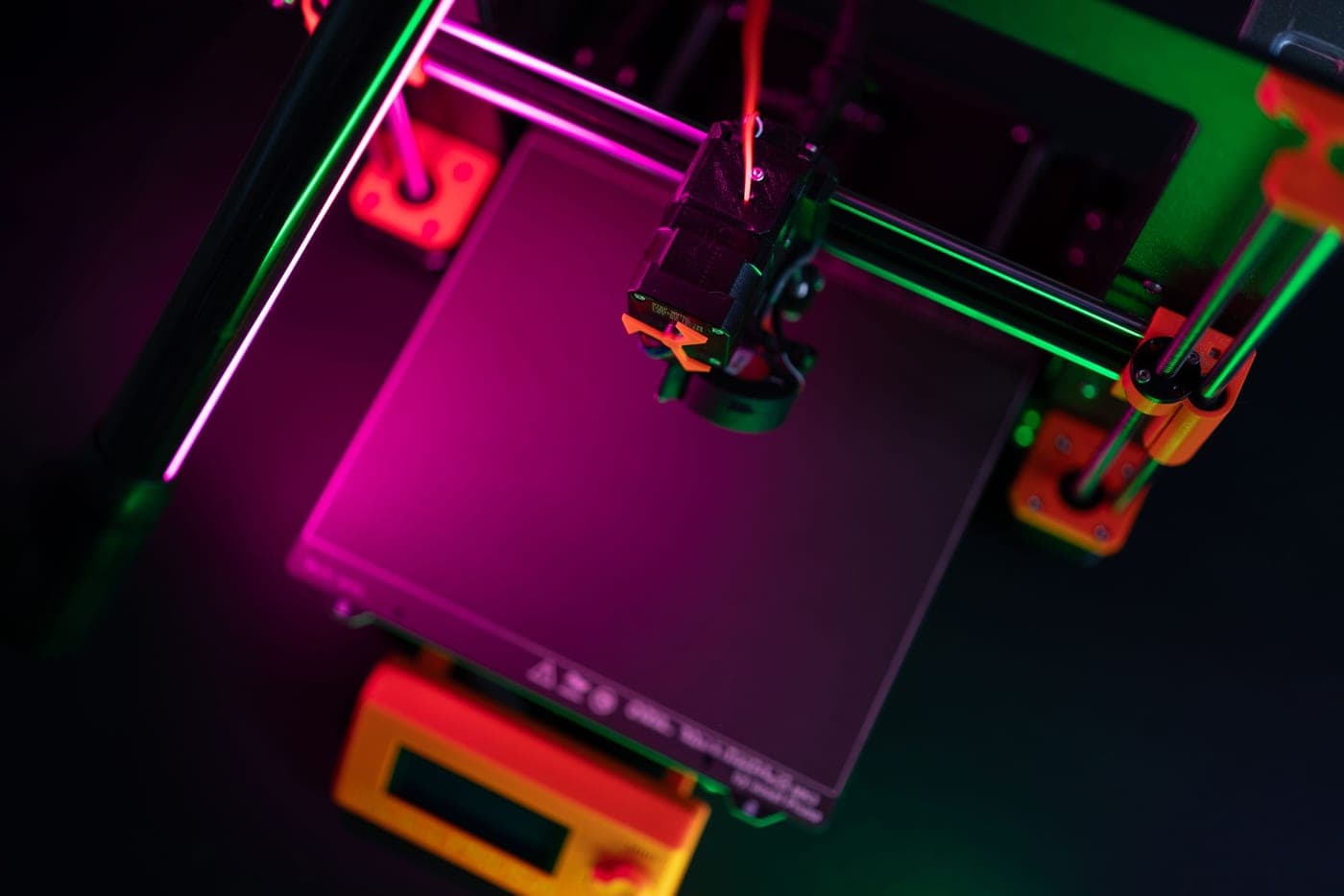 A desktop 3D printer lit against a dark background, part-way through a print