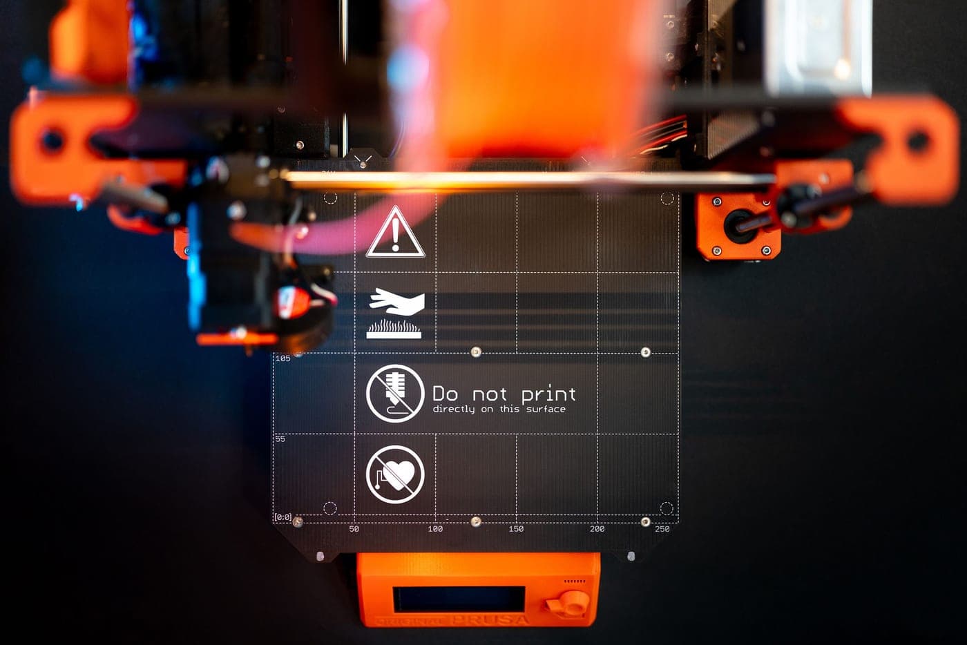 A desktop 3D printer mid-print in a dark room, the print head lit from above